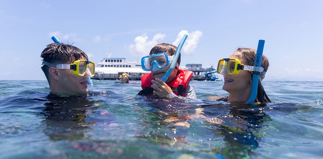 Family snorkelling in ocean with boat behind them
