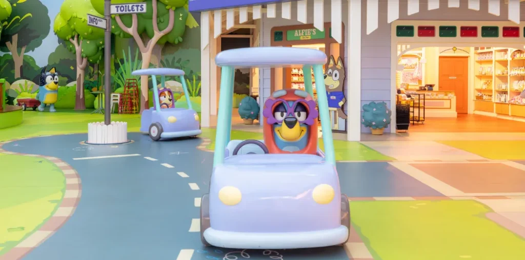 Bluey and Bingo dressed as Granny in Granny carts in Bluey's World Neighbourhood